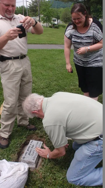 Volunteers placing and photographing a memorial marker in the grass