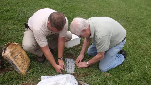 Two men kneeling on the grass setting a memorial marker