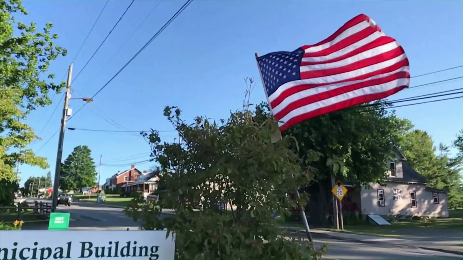 An American flag flying on a pole beside a town street on a sunny day