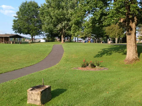 A paved walking path curving across a green lawn under shade trees