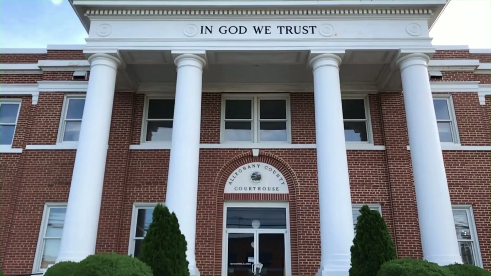 A brick courthouse with white columns and the words IN GOD WE TRUST above the entrance
