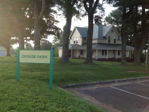 The Crouse Park sign with the Crouse House behind the trees
