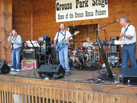A band playing on the Crouse Park Stage under its sign